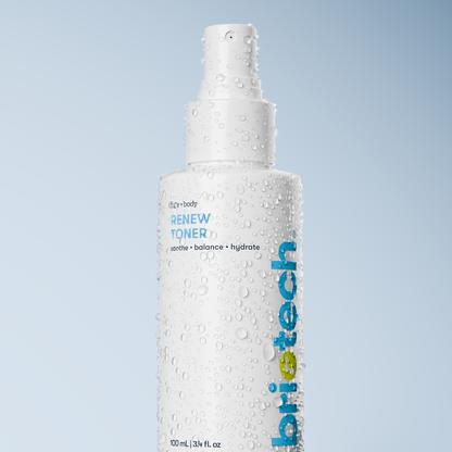 A white Renew Toner spray bottle covered in water droplets sits against a light blue gradient background—ideal as a refreshing mist to calm redness and reduce blemishes.