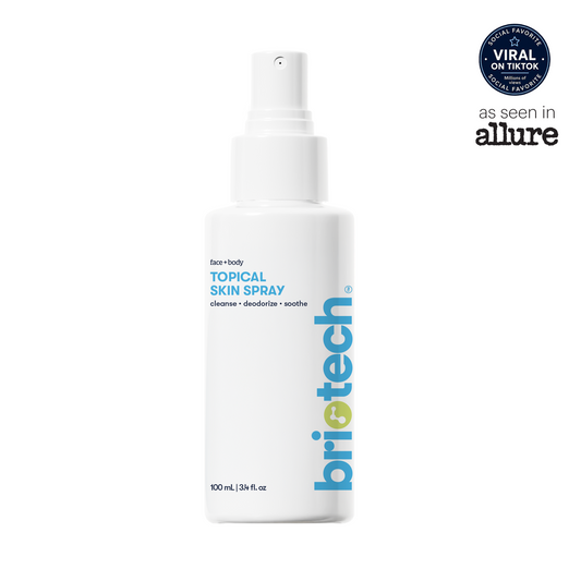 A white 100ml bottle of Briotech Topical Skin Spray featuring blue and green labeling and a spray nozzle. The packaging highlights its TikTok viral status and Allure feature. This soothing spray, formulated for face and body, helps calm irritation and reduce blemishes.